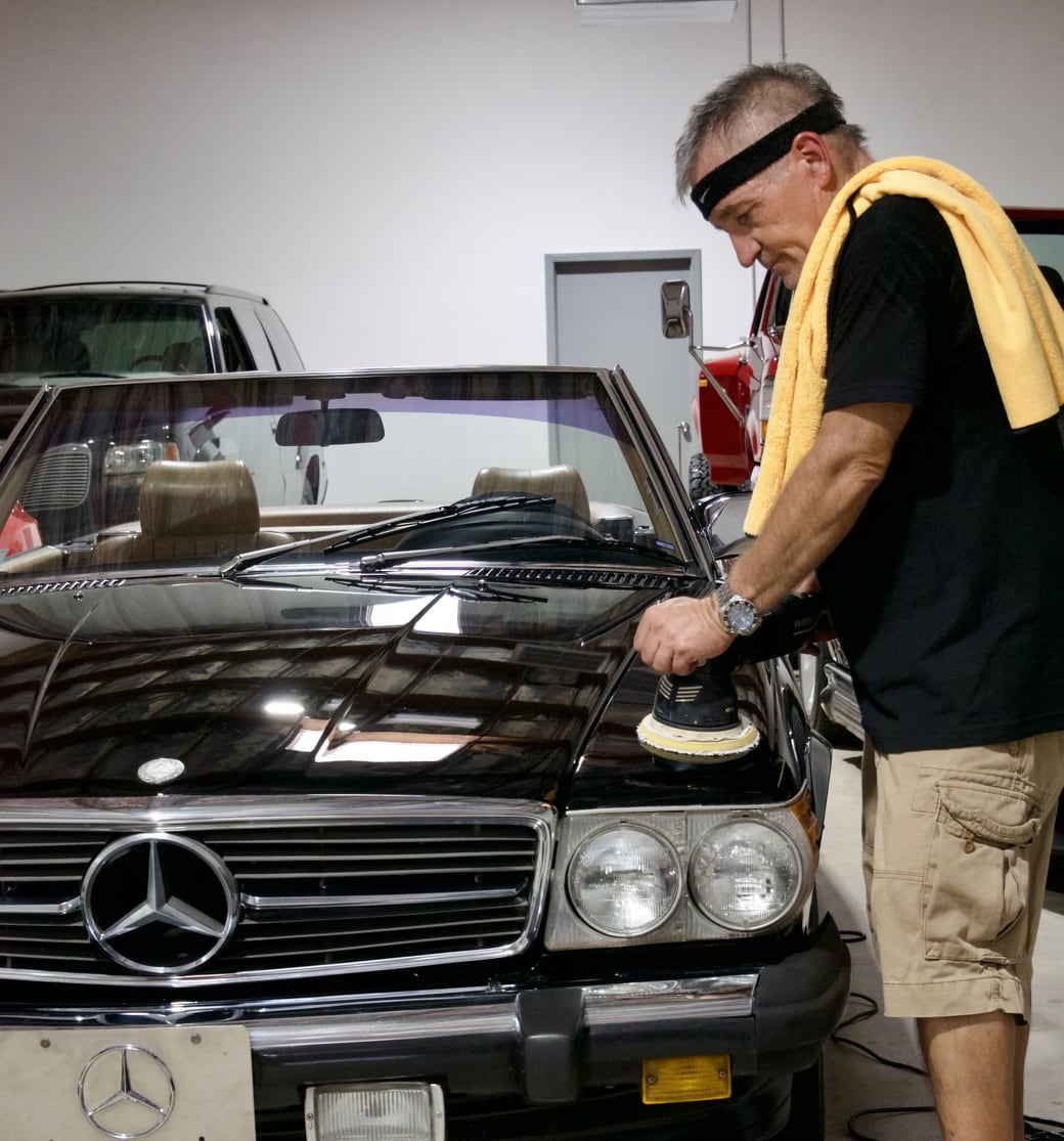 Mike polishing the hood of a classic black Mercedes convertible